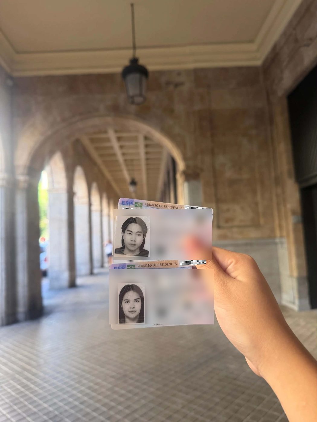 Two Spanish residence permit cards held up under a stone arcade, personal details blurred